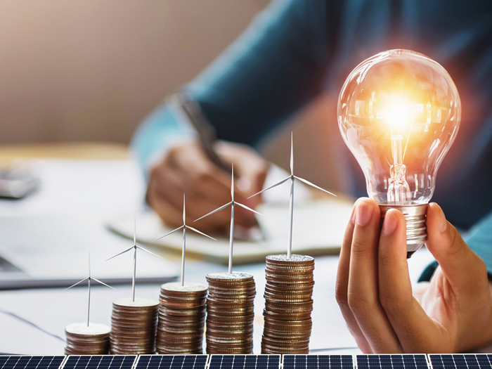 Person holding lightbulb behind solar panels on desk with stacked up coins