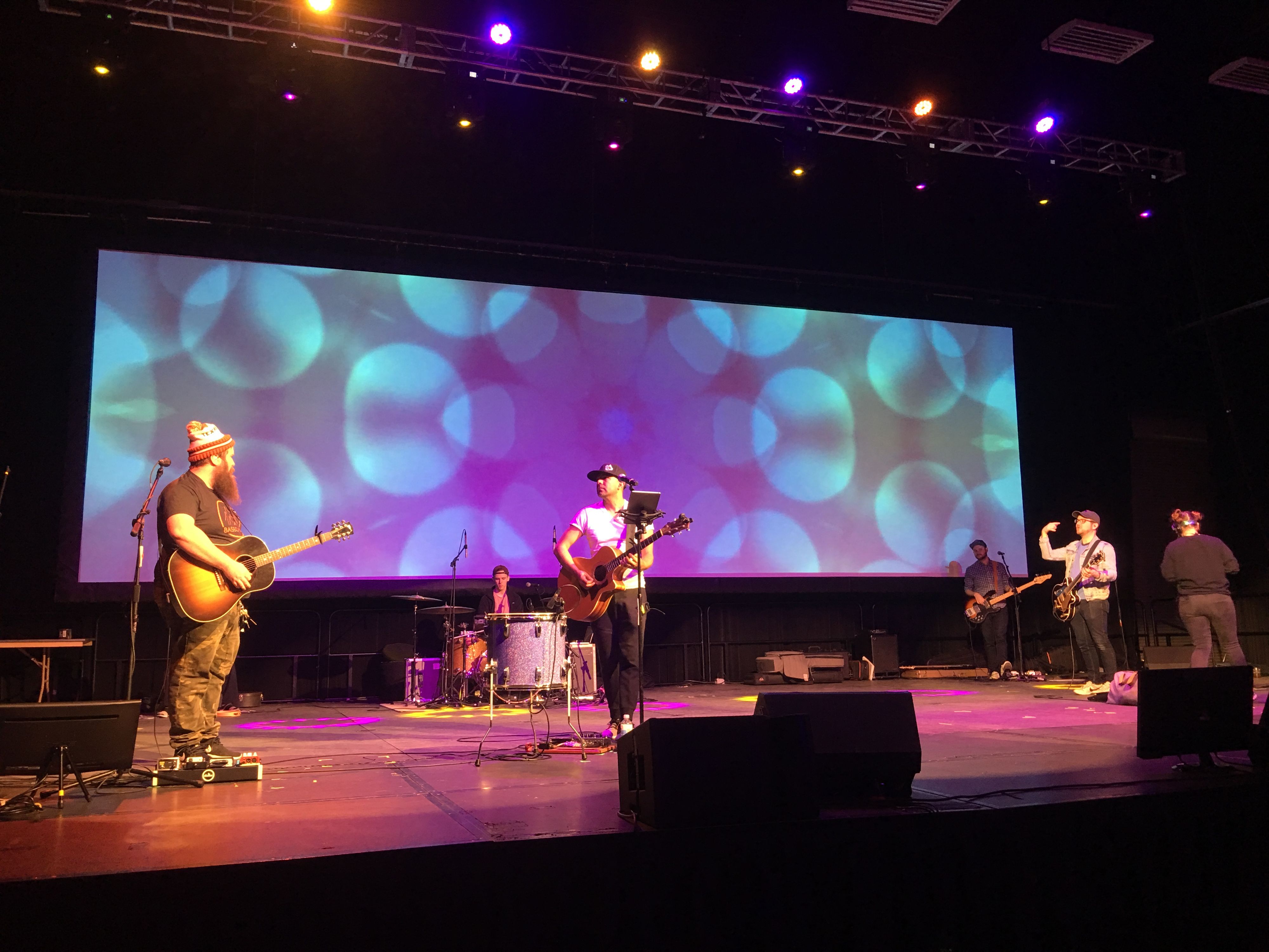 A band playing on stage in front of a large projection display at a St. Louis Conference