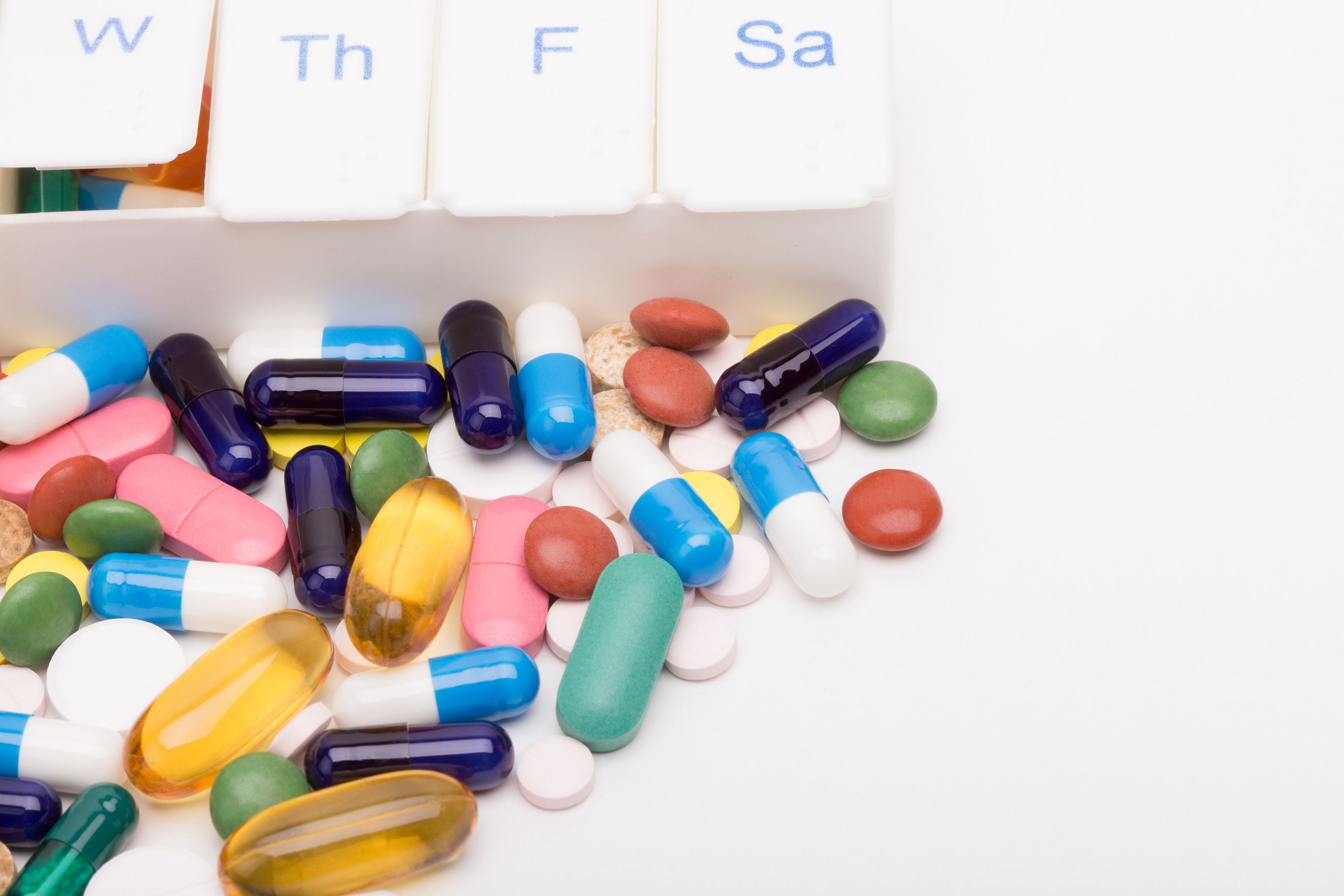 Colorful pills spilled in front of a pill organizer. Medication Compliance