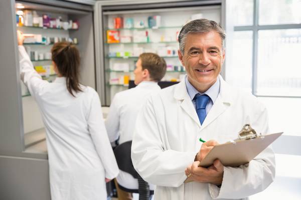 Pharmacist smiling while holding a clipboard with two pharmacists in the background
