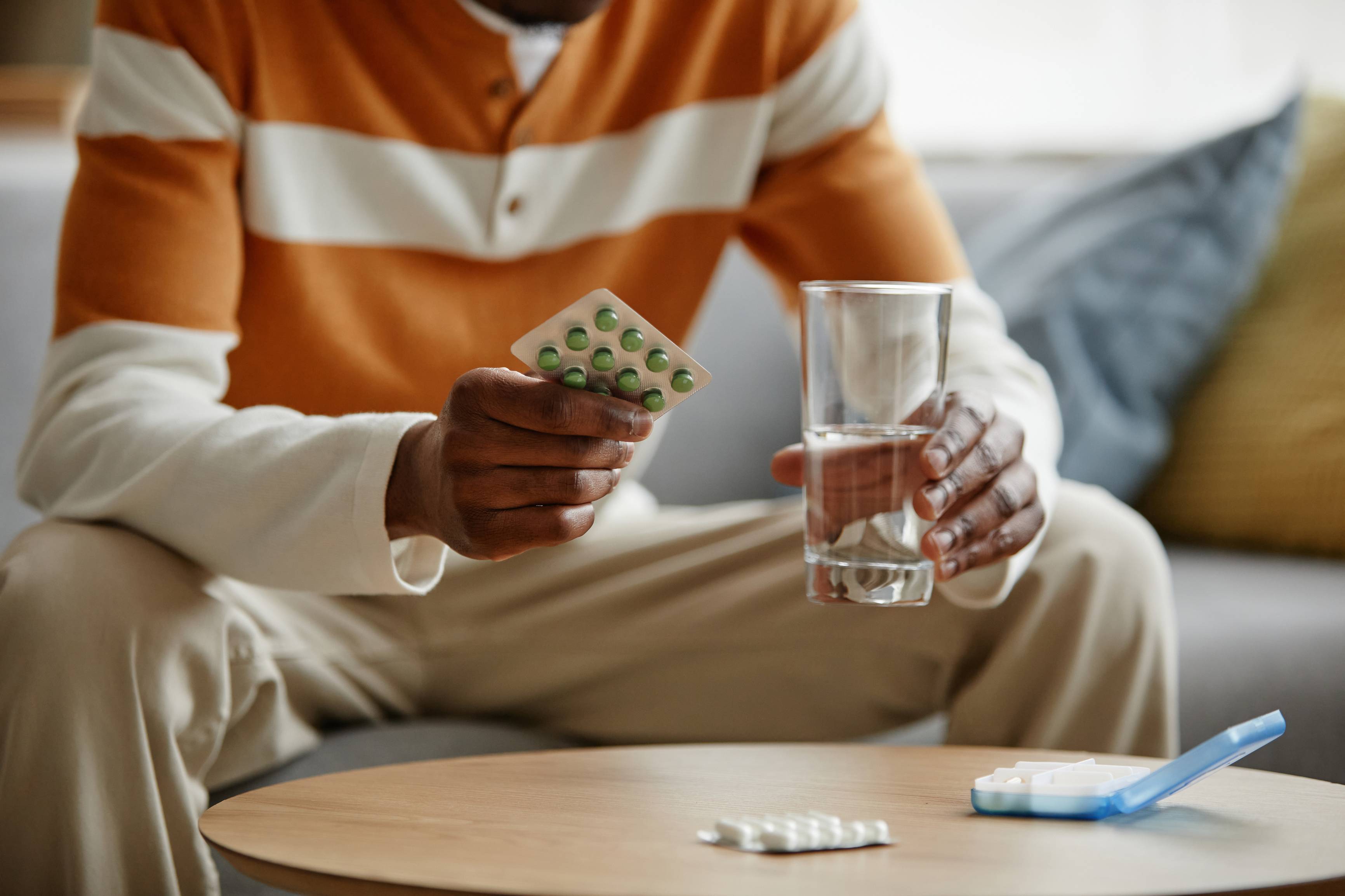 Person sitting on couch holding water and medication