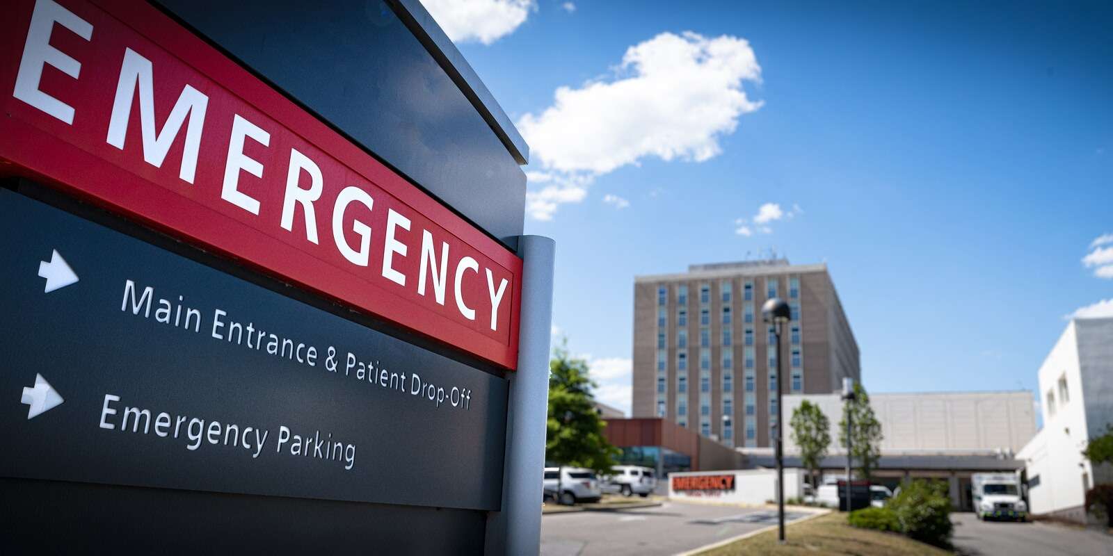 Hospital emergency entrance sign with directions for patient drop-off and parking, with the hospital building in the background.