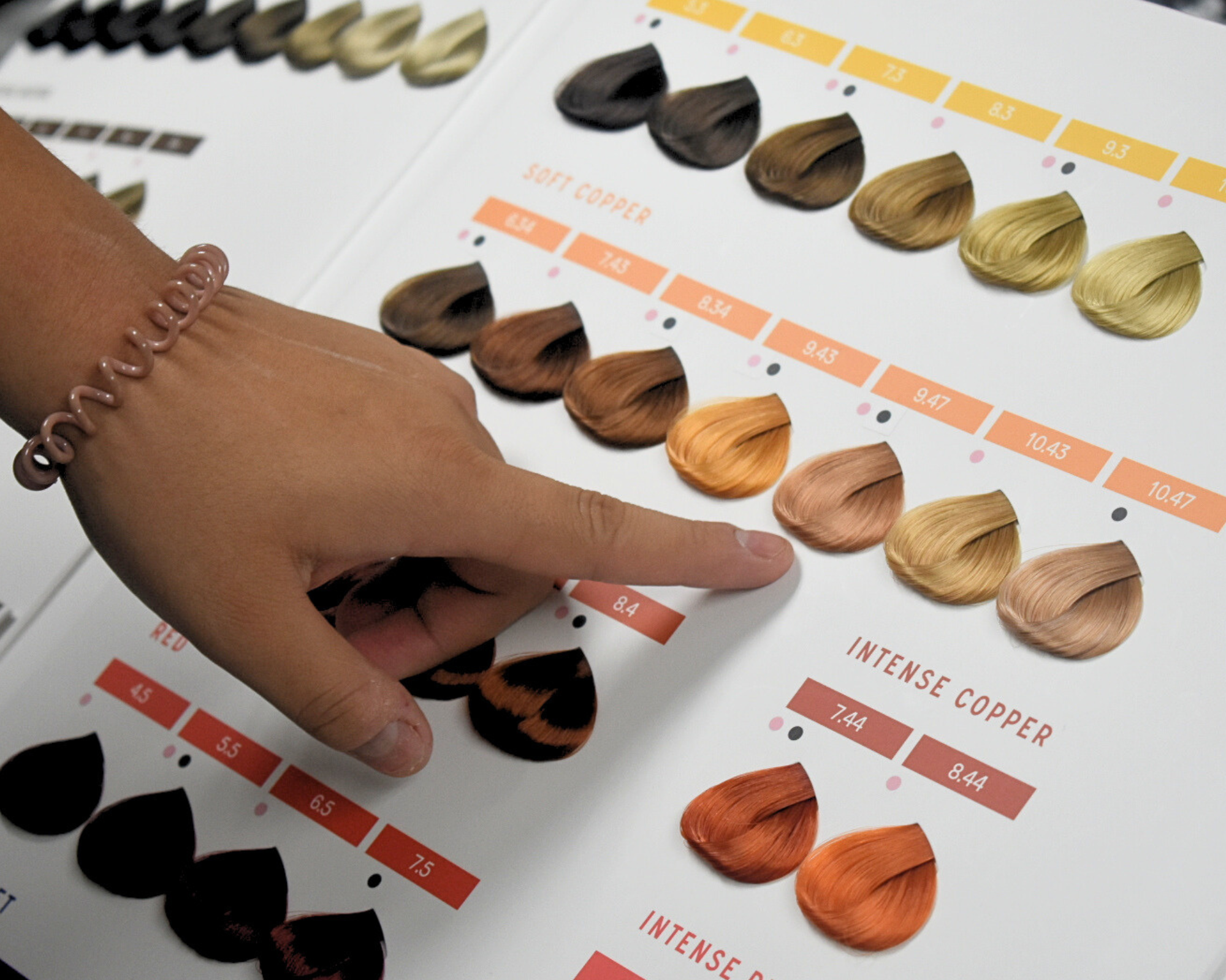A stylist’s hand points to copper shades in a color chart, representing custom color consultations and professional hair artistry at Haus of FIDI in Pensacola. Hair color swatch chart with stylist pointing at copper tones