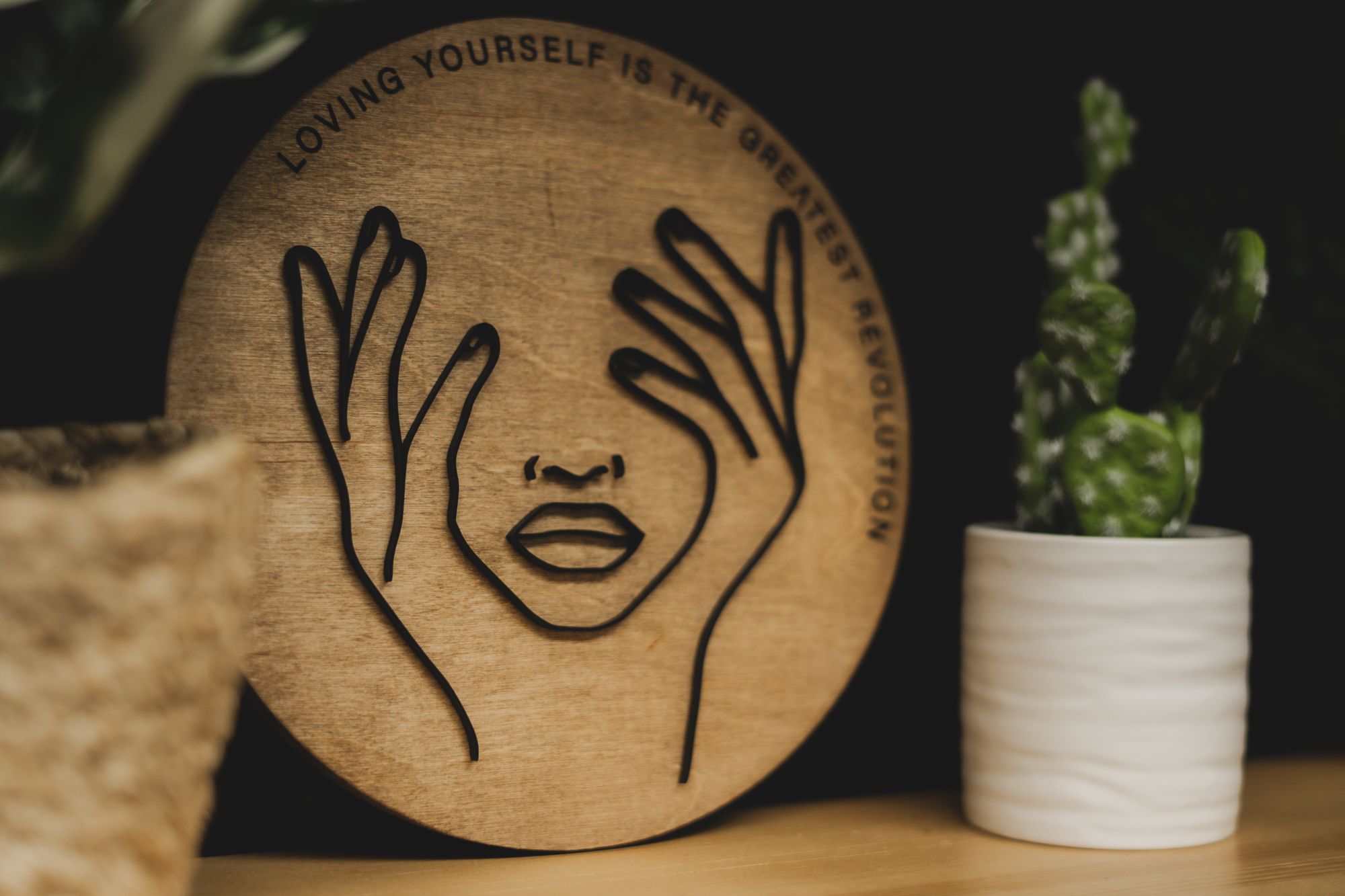 Wooden round art piece with a minimalist face outline and the quote “Loving yourself is the greatest revolution,” displayed as salon decor at Haus of FIDI in Pensacola, promoting self-love and empowerment. fidi-loving-yourself-salon-decor-pensacola.jpg