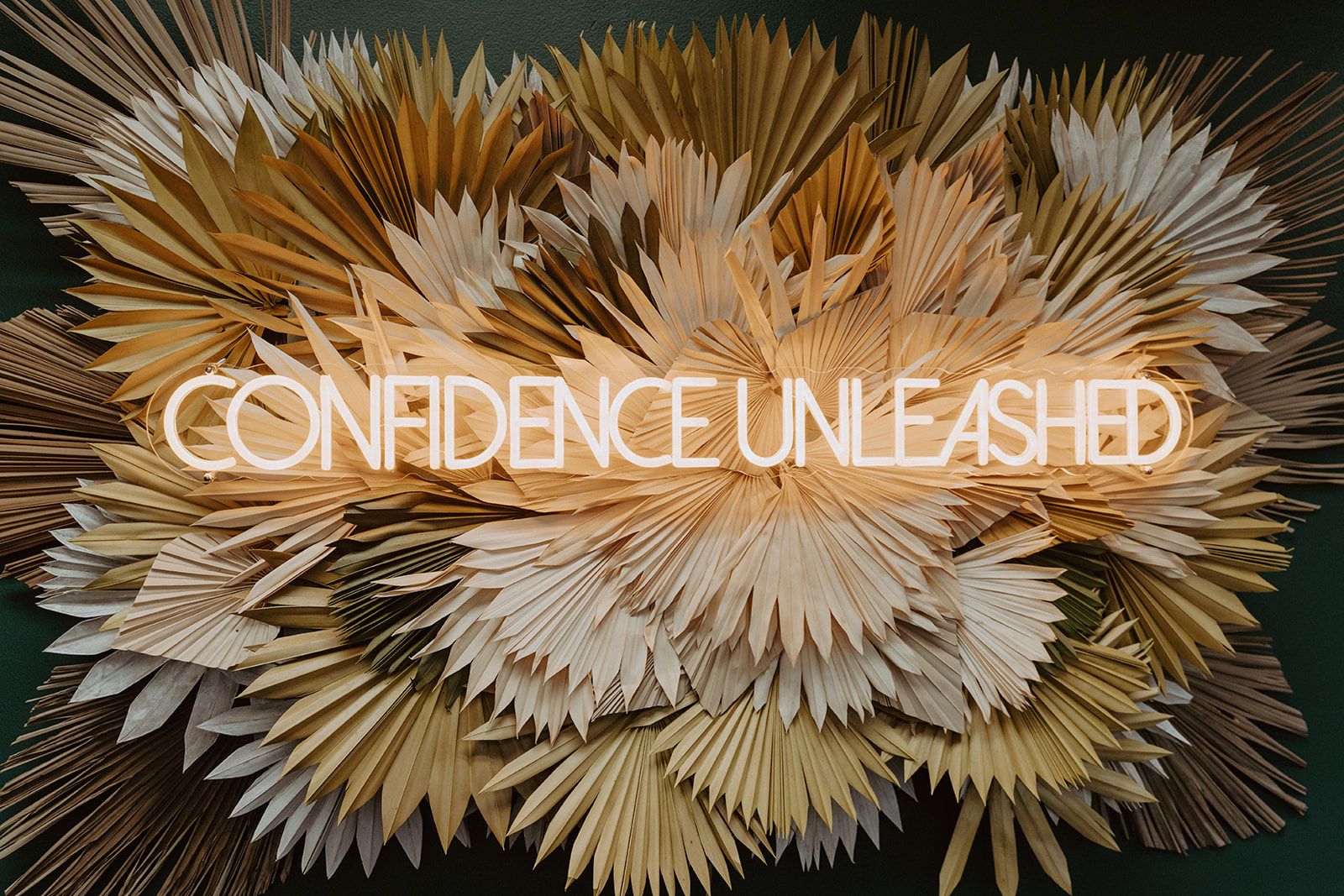 Floral feature wall with neon “Confidence Unleashed” sign at Haus of FIDI in Pensacola, serving as a photo backdrop that symbolizes beauty, empowerment, and self-care. Confidence unleashed