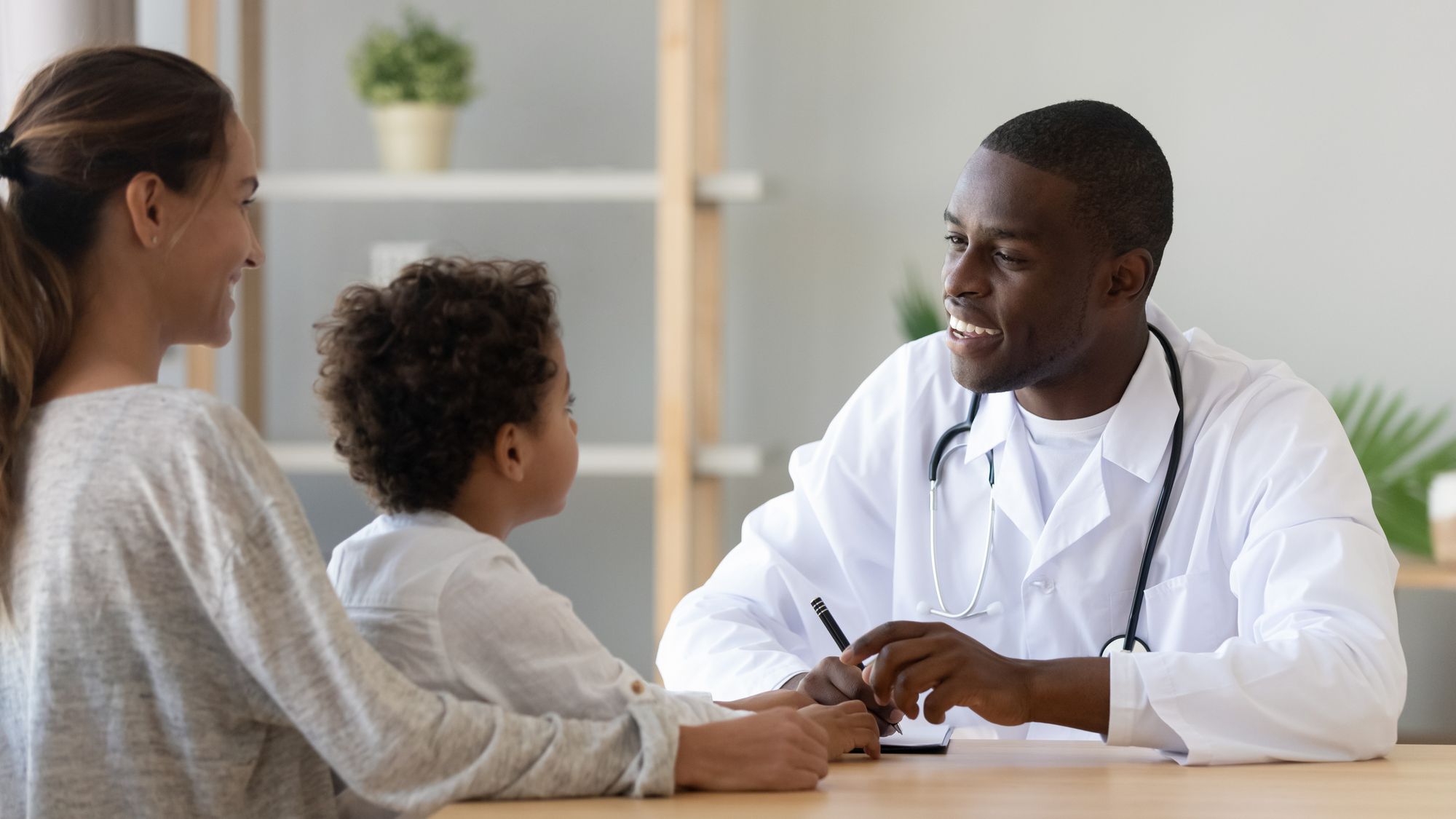 Smiling black male doctor listening to little patient make notes