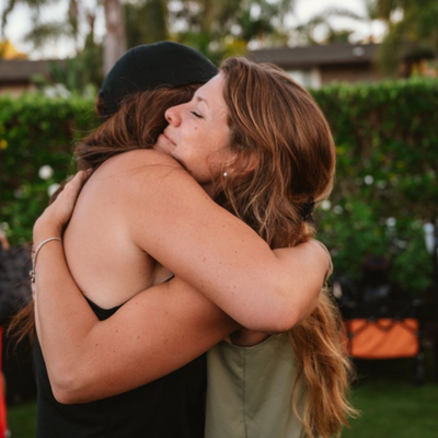 Two young women hugging with expressions of relief.png