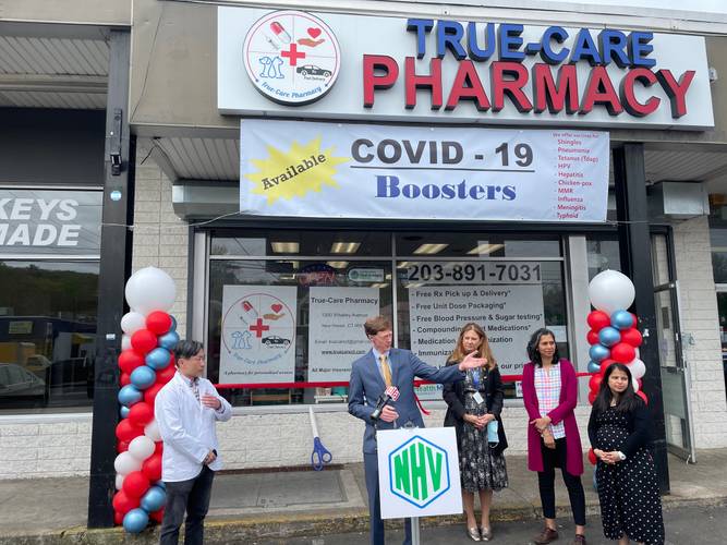 A man in a suit stands in front of a microphone with three women to his right and a pharmacist to his left Pharmacy Interview