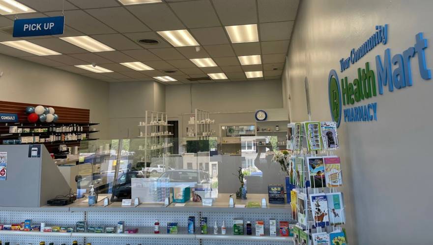 A pharmacy counter with a pick up sign and the wall has a sign that says Health Mart Pharmacy Pick Up Counter