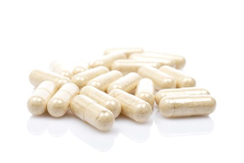 A large amount of capsules filled with a beige powder on a white, reflective surface and white background Capsule Image