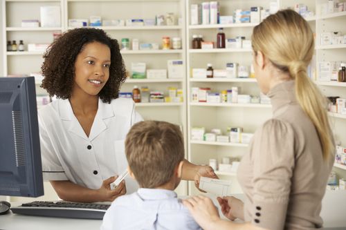 Woman pharmacist receiving a paper from a mother with her left hand on her son's shoulder Pharmacist and patients