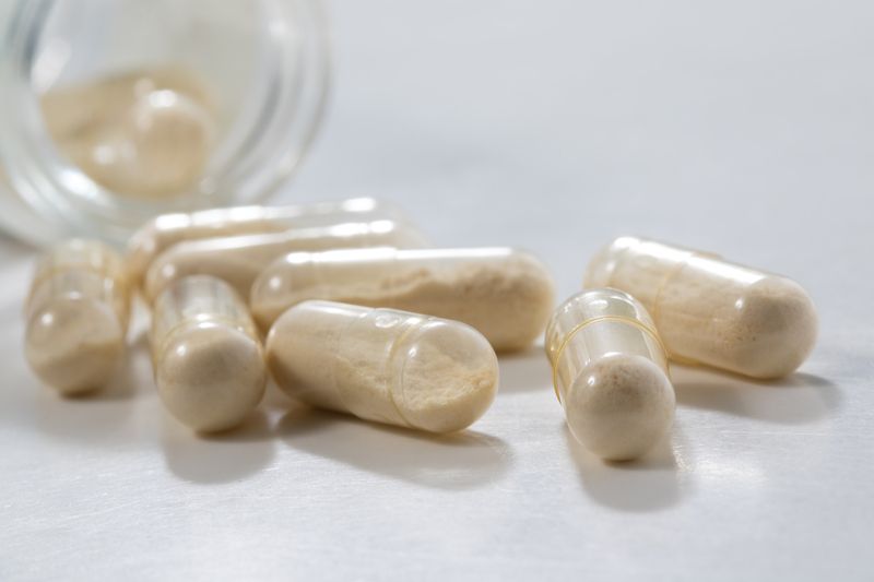 8 capsules filled with a beige powder next to an open bottle Powder Capsules