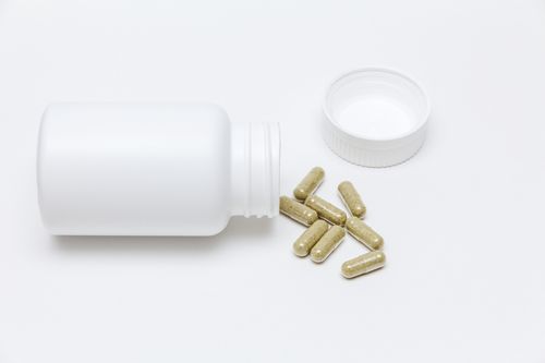 White bottle turned horizontally with dark green capsules spilling out on the white background Capsule spilling out of bottle