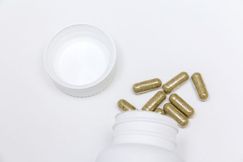 Capsules filled with a dark green powder spilling out of a white bottle on a fully white background Capsules spilling out of Bottle