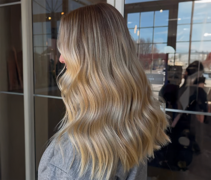 Woman standing in front of window facing away from camera with long champagne blonde hair Long champagne blonde hair