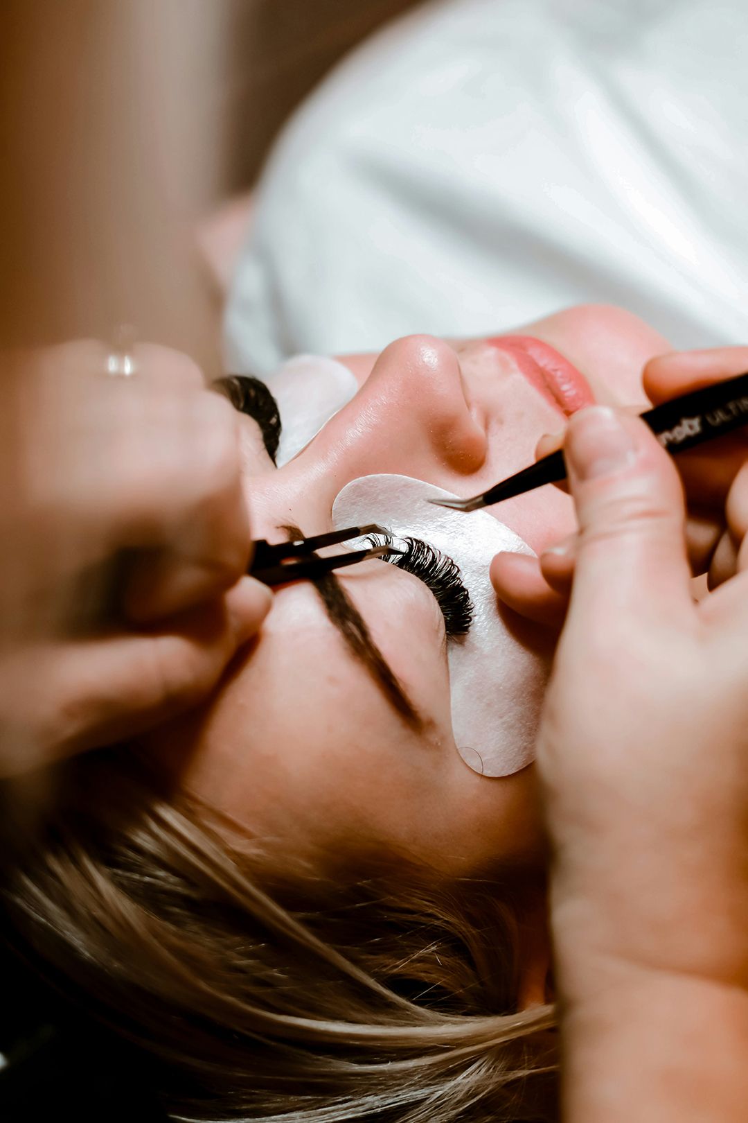 Woman laying on back with eyes closed mid eyelash extension service Eyelash Extensions Image