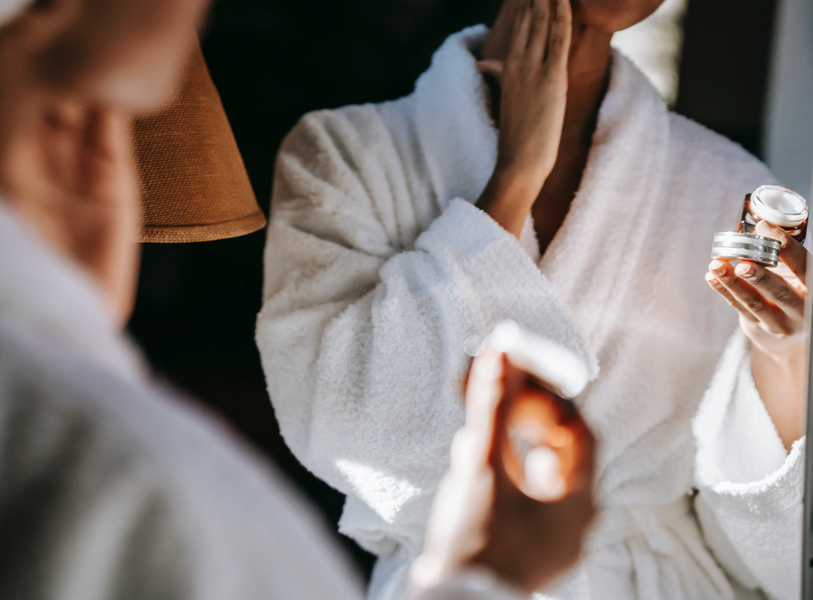 woman in bathrobe facing mirror applying face cream spa image of woman applying face cream