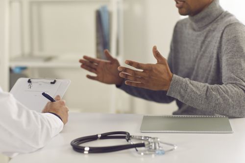 Black man patient sitting and explaining health complaints to man doctor